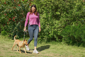 a woman in a purple top and dark jeans walking outside with a small mixed dog on a leash